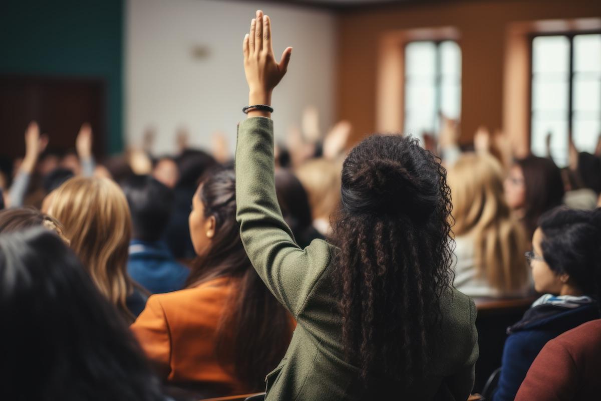 Rear view of black female student raising her hand to ask questions during classroom lecture